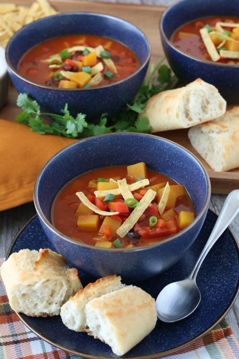 A serving of butternut squash chili in a bowl with a spoon and some bread, ready to be enjoyed. 