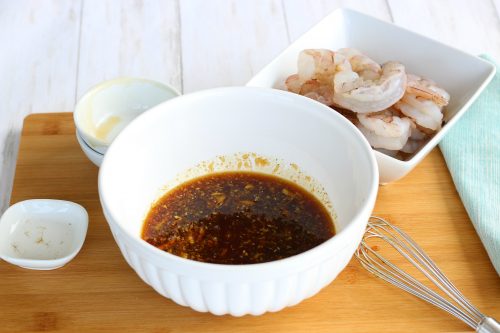 Honey garlic shrimp sauce in a bowl with raw shrimp in a dish next to it waiting to be prepared. 