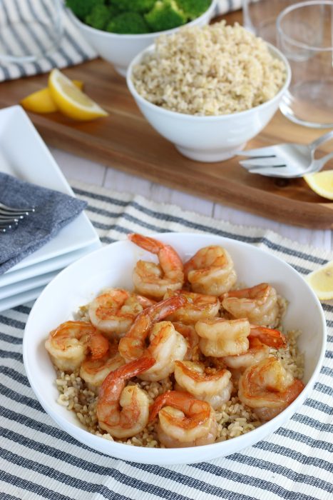 Plated and ready to eat the honey garlic shrimp are over a bed of brown rice set on a beautiful table with utensils. Healthy dinner recipes ready to enjoy. 